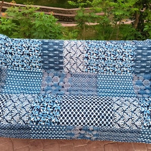 Könnte beinhalten: Eine blau-weiß gemusterte Sofahusse. Die Hülle hat ein Patchwork-Design mit verschiedenen floralen und geometrischen Mustern in Blau- und Weißtönen. Die Sofahusse besteht aus einem weichen, strukturierten Stoff.