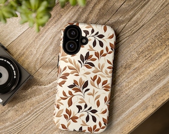 May include: A phone case with a cream background and a repeating pattern of brown and tan leaves and branches. The case has a dual-lens camera cutout and is resting on a wooden surface.