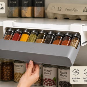 May include: A gray under-shelf spice rack organizer featuring a pull-out drawer design. The unit holds nine clear glass spice jars with metallic lids, each filled with various colorful spices. The rack is mounted to a white shelf surface.