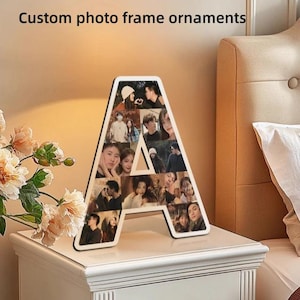 Könnte beinhalten: Ein hölzernes Foto-Rahmen-Ornament in Form des Buchstabens "A", gefüllt mit mehreren Fotos. Der Rahmen hat einen weißen Rand und steht auf einem weißen Nachttisch. Der Text "Custom photo frame ornaments" befindet sich oben im Bild.