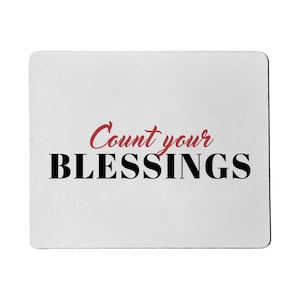 Puede incluir: Alfombrilla de ratón rectangular blanca con las palabras "Count your BLESSINGS" en escritura negra y roja. La alfombrilla tiene esquinas redondeadas y una superficie lisa.