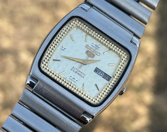 Seiko 5 automático vintage de 23 joyas, esfera de 33 mm, día y fecha en inglés y árabe, esfera dorada texturizada y anillo de horas dorado.