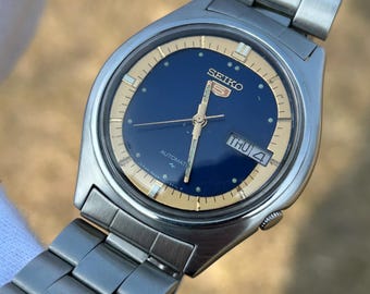 Reloj Seiko 5 automático vintage de 37 mm / Esfera azul con anillo de capítulos dorado / Indicador de día y fecha en inglés y árabe / Brazalete de acero inoxidable / Seiko clásico