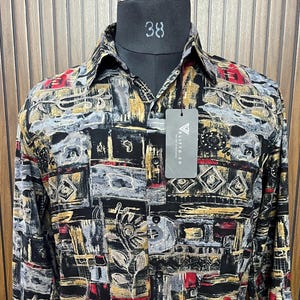Puede incluir: Camisa de manga larga con un estampado geométrico en negro, gris, rojo y dorado. La camisa se exhibe en un maniquí negro con el número 38 en el cuello. Una etiqueta con el texto "ELITTO.CO" cuelga de la camisa.