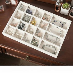 May include: A white jewelry organizer filled with various rings, bracelets, and necklaces. The organizer has multiple compartments, each holding a different piece of jewelry. The jewelry includes silver, gold, and pearl pieces.