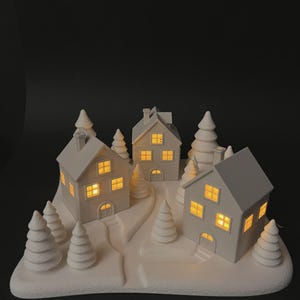 Puede incluir: Una escena de pueblo navideño de cerámica blanca con tres casas iluminadas y varios árboles de pino estilizados. Las casas tienen ventanas y puertas amarillas brillantes. La escena está sobre una base blanca con un camino sinuoso.