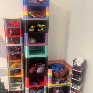 Könnte beinhalten: Eine Sammlung farbenfroher Aufbewahrungsboxen, die in verschiedenen Konfigurationen gestapelt sind. Die Boxen sind mit Socken, Krawatten und anderem Zubehör gefüllt. Die Boxen sind in Regenbogenfarben gehalten, darunter Rot, Blau und Grün. Das Thema ist Organisation.
