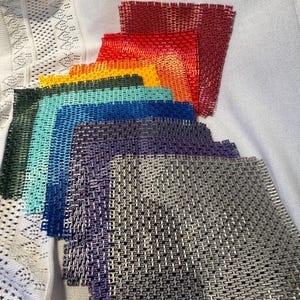 May include: A collection of square, mesh-like fabric swatches arranged in a cascading fan pattern. The colors include red, orange, yellow, teal, blue, purple, and silver. Each square features a consistent, repeating grid-like texture.
