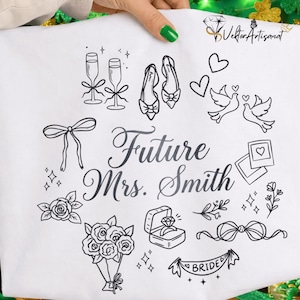 May include: White fabric with black line art illustrations of wedding-related items, including champagne glasses, shoes, doves, hearts, a ring, and a banner that says "Bride." The text "Future Mrs. Smith" is also displayed.