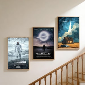 Peut inclure: Trois affiches encadrées du film "Interstellar" sont accrochées à un mur beige. Les affiches présentent des images d'un astronaute, d'un trou noir et d'un lancement de fusée. Les affiches sont dans des cadres en bois.