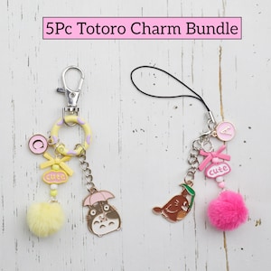 May include: A bundle of five Totoro charms. One charm is attached to a silver keychain with a yellow ring, a yellow pom-pom, and a Totoro character. The other charm has a pink pom-pom and a brown character. The text "cute" is visible.