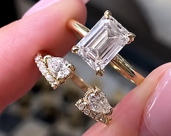 May include: A gold ring featuring a large emerald-cut center stone and a second gold ring featuring two pear-shaped stones accented with small round pavé diamonds. Both rings have thin, polished gold bands and clear, faceted gemstones.