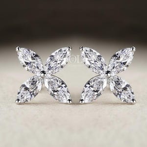 May include: A pair of elegant stud earrings. Each earring features a four-petal flower design, with each petal composed of a marquise-cut, clear gemstone. The earrings are set in a silver-colored metal.