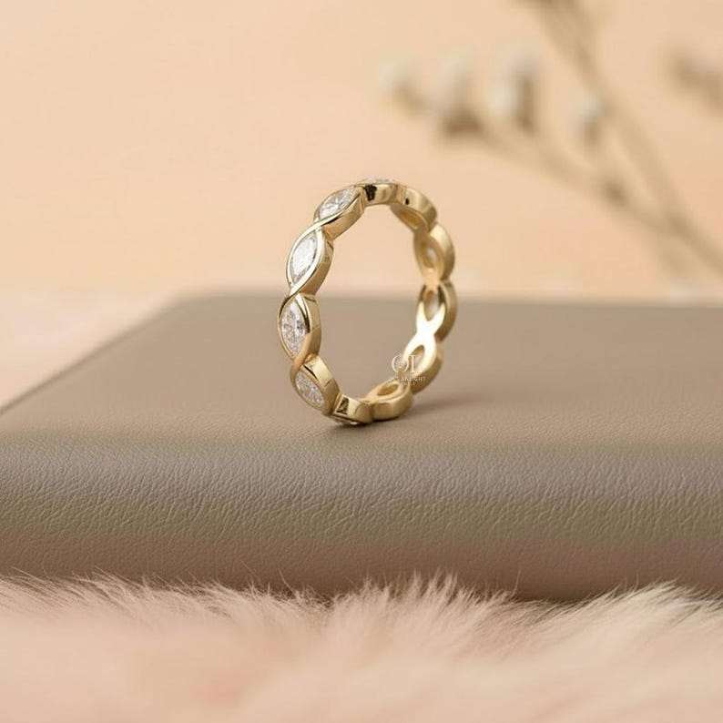 May include: A gold ring with a repeating pattern of marquise-cut gemstones. The ring is set with clear, sparkling stones and has a polished, yellow gold band. The ring is displayed on a neutral-toned surface.