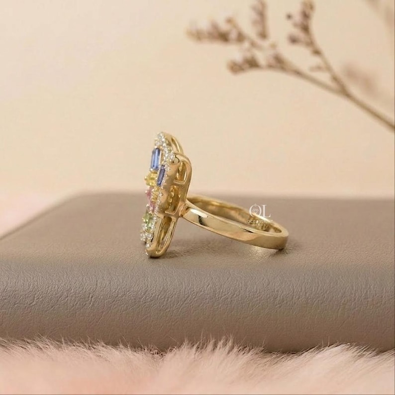 May include: A gold ring featuring a cluster of multi-colored baguette and round-cut gemstones, including blue, yellow, pink, and green stones. The ring has a polished gold band and a decorative setting that holds the array of colorful gems.