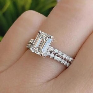 May include: A close-up of a diamond ring set. The ring features a large, rectangular emerald-cut diamond as the centerpiece, with a band of smaller diamonds. A second band of smaller diamonds is also visible.