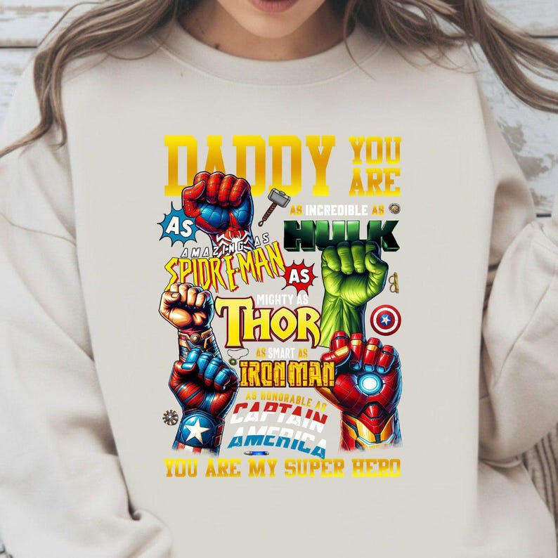 May include: Cream-colored sweatshirt with a graphic featuring superhero fists and text. The text includes "Daddy You Are" and references to Spiderman, Hulk, Thor, Iron Man, and Captain America. The phrase "You Are My Super Hero" is also present.