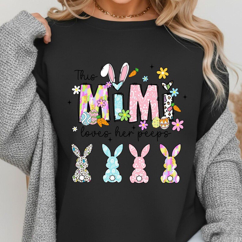 May include: Black sweatshirt with the text "This Mimi loves her peeps" in colorful letters and Easter-themed graphics. The design includes bunny ears, carrots, flowers, and four bunny silhouettes in a row.