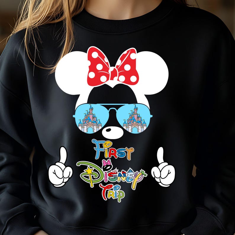 May include: Black sweatshirt featuring a Minnie Mouse design with a red polka dot bow, sunglasses reflecting a castle, and the text "First Disney Trip." White gloved hands point upwards on either side of the text.