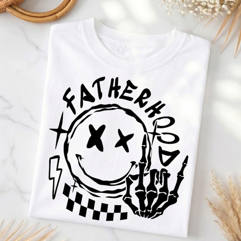 May include: White t-shirt with a black graphic. The graphic features a smiley face with X eyes, a skeleton hand giving the middle finger, and the words "FATHERHOOD" and "BAD". A lightning bolt and checkered square are also included.