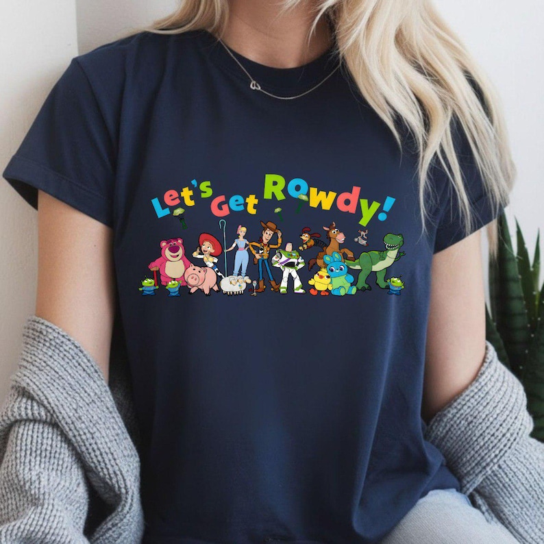 K&ouml;nnte beinhalten: Marineblaues T-Shirt mit dem bunten Schriftzug "Let's Get Rowdy!" &uuml;ber Cartoonfiguren. Zu den Figuren geh&ouml;ren ein rosa B&auml;r, ein Schwein, ein Alien und ein Cowboy.