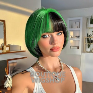 May include: A woman with blue eyes and a pearl necklace is wearing a two-tone wig. The wig has a green top and black underneath. The text "BOUTIQUE WIGSHOP" is superimposed on the image.