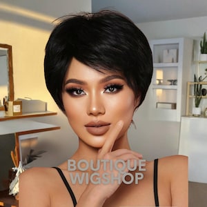 Peut inclure: Une femme portant une perruque courte noire et superposée. La perruque a une raie sur le côté et encadre le visage. L'image comprend le texte "BOUTIQUE WIGSHOP". La femme porte un haut noir.