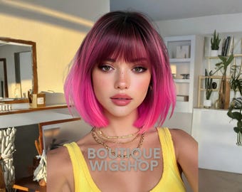 May include: A woman with a short, pink and burgundy wig with a fringe. She is wearing a yellow top and layered gold necklaces. The text "BOUTIQUE WIGSHOP" is visible on the top.