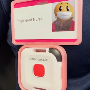 Peut inclure: Un porte-badge rose avec une carte blanche indiquant "Infirmière agréée" et une photo d'un emoji masqué. En dessous, un appareil blanc et rose avec un bouton rouge et le texte "kontakt.io".
