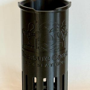 May include: A black 3D-printed cup holder with a handle and vertical slots. The holder features the text "Treasure Coast 3D Creations" and a tropical scene with a palm tree and lighthouse.