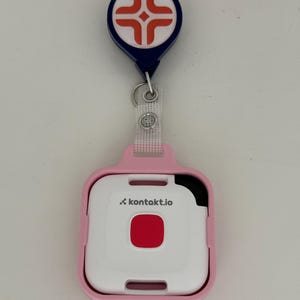 May include: A pink and white medical alert device with the text "kontakt.io" and a red button. The device is attached to a blue and white badge reel with a medical symbol.