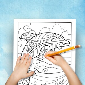 May include: A black and white colouring page featuring a detailed illustration of a dolphin with a smiling face. The dolphin is surrounded by waves and bubbles. A hand is holding a yellow pencil and colouring the dolphin.
