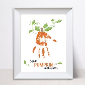 Pode incluir: Impressão emoldurada com uma impressão de mão laranja transformada em abóbora, com folhas e vinhas verdes. O texto "Cutest PUMPKIN in the patch" está abaixo. A obra de arte tem um fundo branco.