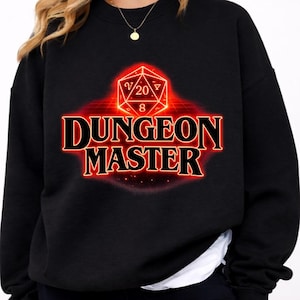 Könnte beinhalten: Schwarzes Sweatshirt mit einem roten und orangefarbenen Aufdruck "DUNGEON MASTER". Die Grafik zeigt einen D20-Würfel mit den Zahlen 20 und 8. Das Sweatshirt hat einen Rundhalsausschnitt.
