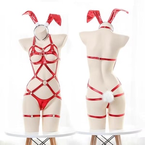 Può includere: Un body a imbracatura rosso metallizzato con design a listini, anelli in metallo, scollo all'americana e una fascia per capelli abbinata con orecchie da coniglio rosse. La vista posteriore mostra una coda bianca soffice sulle cinghie.