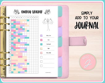 May include: A pink journal with an energy tracker page. The tracker has a grid with color-coded blocks for each day of the month. The text "ENERGY TRACKER" is at the top. The journal also has the text "SIMPLY ADD TO YOUR JOURNAL".