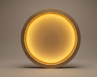 May include: A round, wooden-framed wall sconce with a warm, golden glow emanating from within. The sconce has a simple, minimalist design, with a light-colored wood frame and a soft, diffused light source.