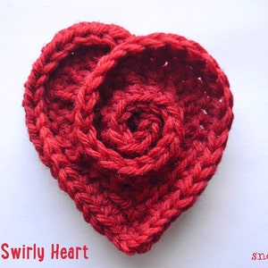 Puede incluir: Un corazón de crochet rojo con un diseño de espiral. El corazón está hecho con punto bajo y tiene un aspecto texturizado. El texto "Pattern Swirly Heart" es visible debajo del corazón.