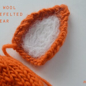 May include: Close-up of a knitted orange ear with white wool needle felted onto the inside. The text "WHITE WOOL NEEDLE FELTED ONTO EAR" is visible above the ear.