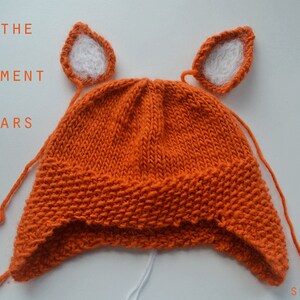 May include: Orange knitted hat with white felt ears attached. The text "FIND THE RIGHT PLACEMENT FOR THE EARS" is visible above the hat.