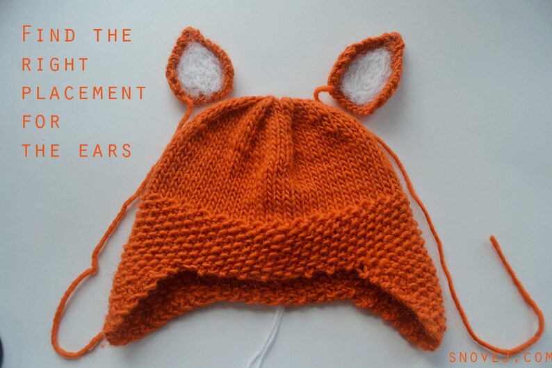 May include: Orange knitted hat with white felt ears attached. The text "FIND THE RIGHT PLACEMENT FOR THE EARS" is visible above the hat.