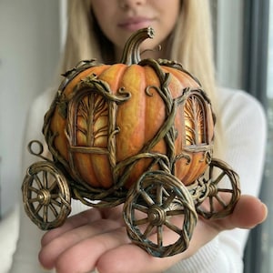 May include: A decorative pumpkin carriage with intricate details. The orange and yellow pumpkin has vine-like accents and four bronze-coloured wheels. The carriage features two arched windows with tree-like designs.