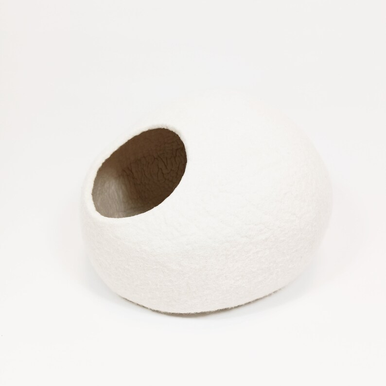 May include: White felt pet bed shaped like a rounded oval with a large opening on one side. The bed is made of a soft, fluffy material.