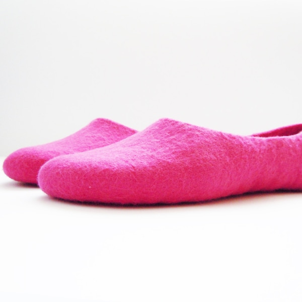 Pode incluir: Um par de pantufas de feltro rosa brilhante. As pantufas têm um design simples e arredondado. O material macio e texturizado sugere conforto e calor, perfeitas para uso em ambientes internos.