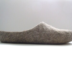 K&ouml;nnte beinhalten: Ein einzelner grauer Filzschuh, im Profil betrachtet. Der Schuh hat eine abgerundete Spitze und einen niedrigen R&uuml;cken, was auf einen bequemen Hausschuh hindeutet. Das Material scheint eine weiche Naturfaser zu sein.