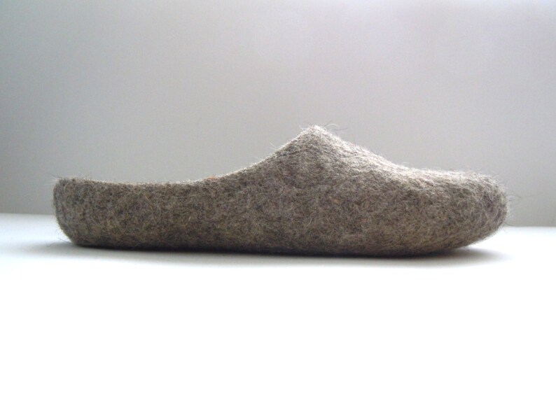 K&ouml;nnte beinhalten: Ein einzelner grauer Filzschuh, im Profil betrachtet. Der Schuh hat eine abgerundete Spitze und einen niedrigen R&uuml;cken, was auf einen bequemen Hausschuh hindeutet. Das Material scheint eine weiche Naturfaser zu sein.
