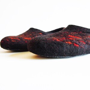 May include: A pair of black felt slippers with red accents. The slippers have a rounded toe and a low profile, suitable for indoor wear. The red detailing adds a pop of color to the otherwise dark design.