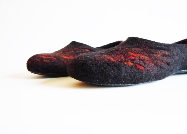 May include: A pair of black felt slippers with red accents. The slippers have a rounded toe and a low profile, suitable for indoor wear. The red detailing adds a pop of color to the otherwise dark design.