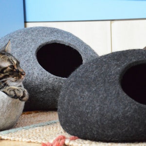 May include: Three gray felt cat beds, one with a cat inside. The beds are shaped like a rounded oval with a hole in the side for the cat to enter.