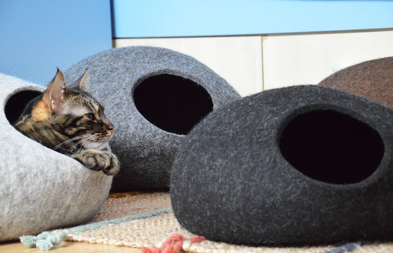 May include: Three gray felt cat beds, one with a cat inside. The beds are shaped like a rounded oval with a hole in the side for the cat to enter.